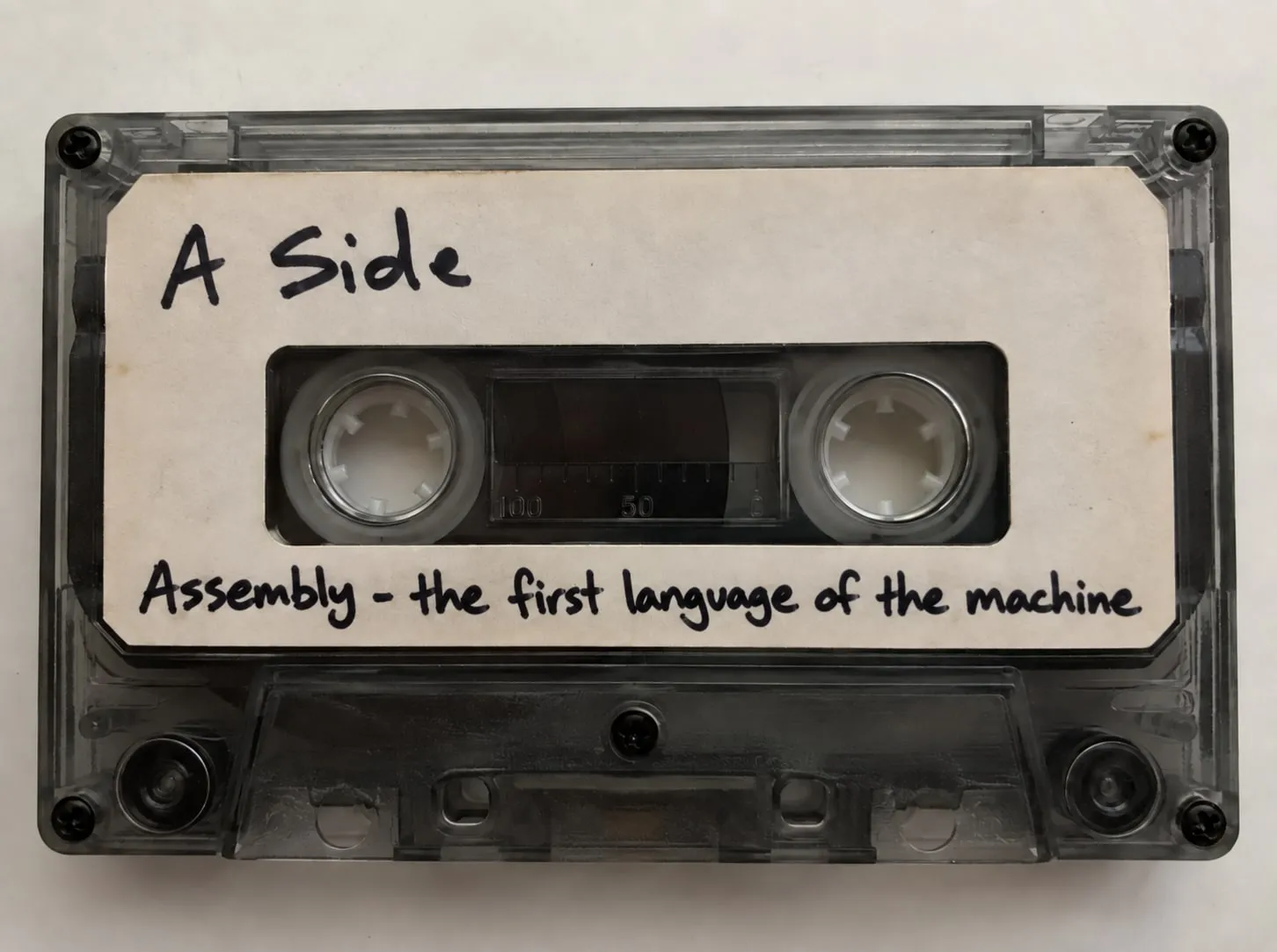 A cassette tape with a handwritten label: "A Side. Assembly - the first language of the machine."